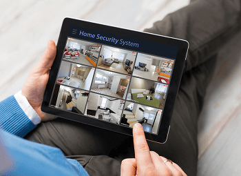 Person laying on a couch reviewing feed from their home security system on a tablet